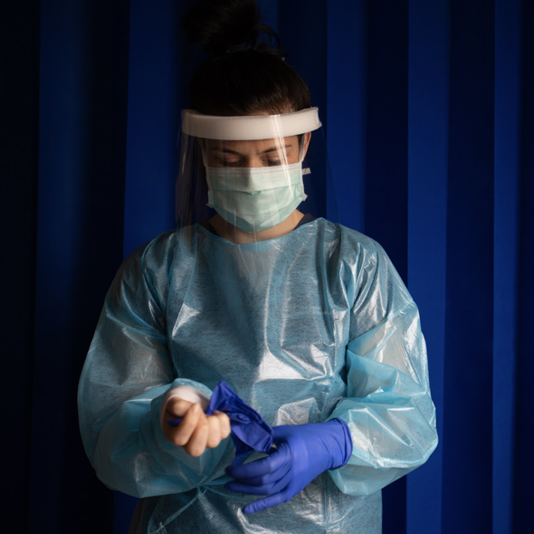 Image of a nurse in scrubs and face protection putting on protective gloves.